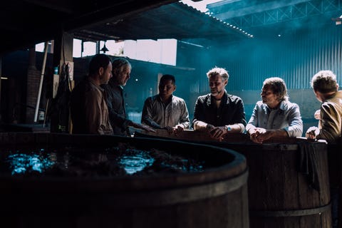group of men standing next to a brewing barrel